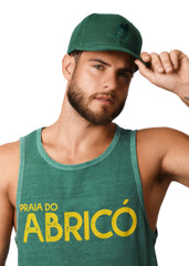 Man wearing a green tank top with 'Praia do AbricĂł' text and a matching cap.